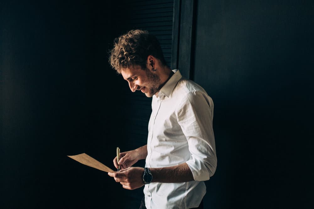 A man smiles while writing on a piece of paper.