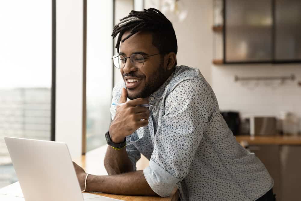 A man smiles while reading a message on his laptop.