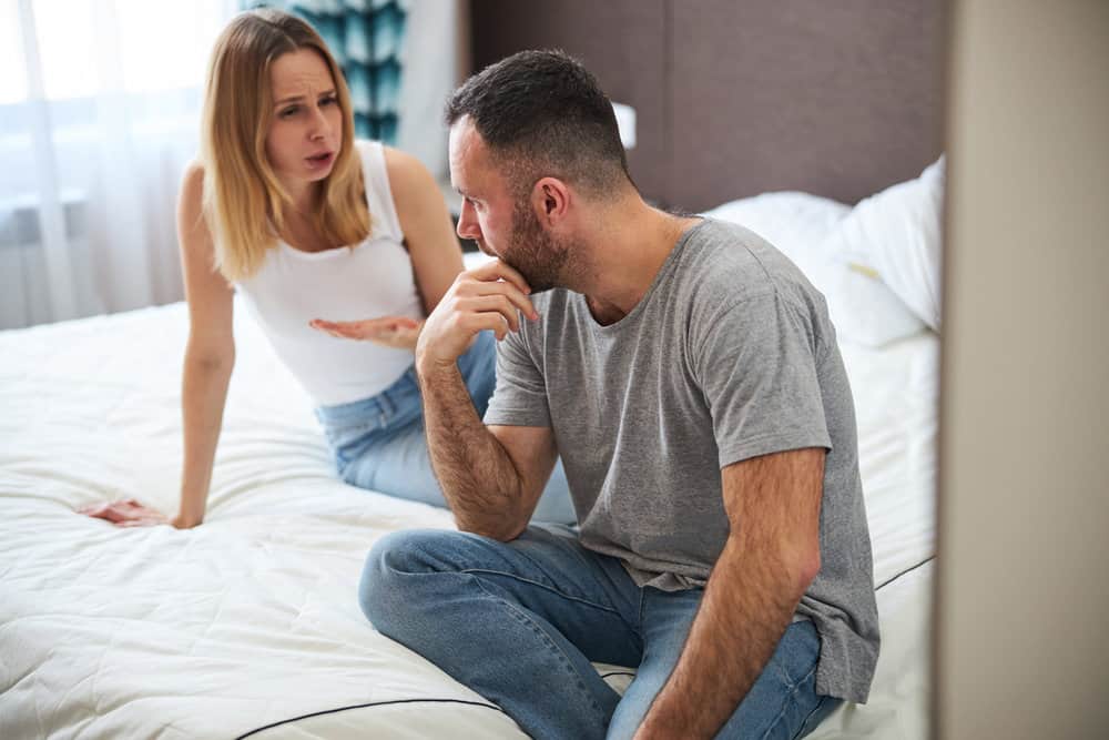 A couple argues indoors while sitting on a bed.