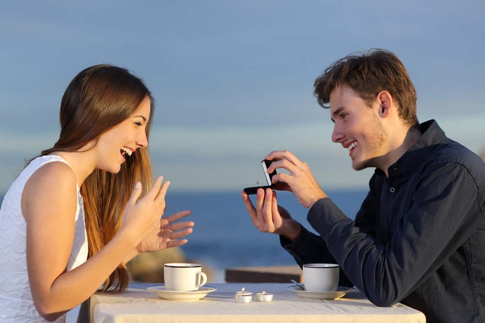 A man proposes to a woman while they both smile drinking coffee.