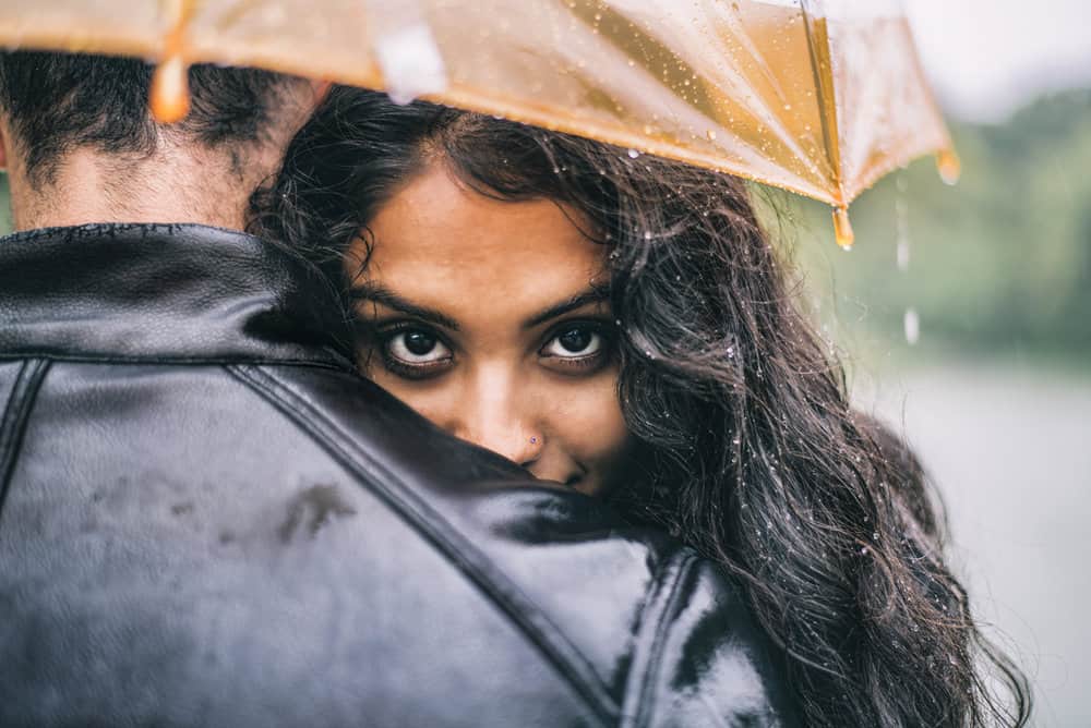 A couple embraces while the man holds an umbrella.