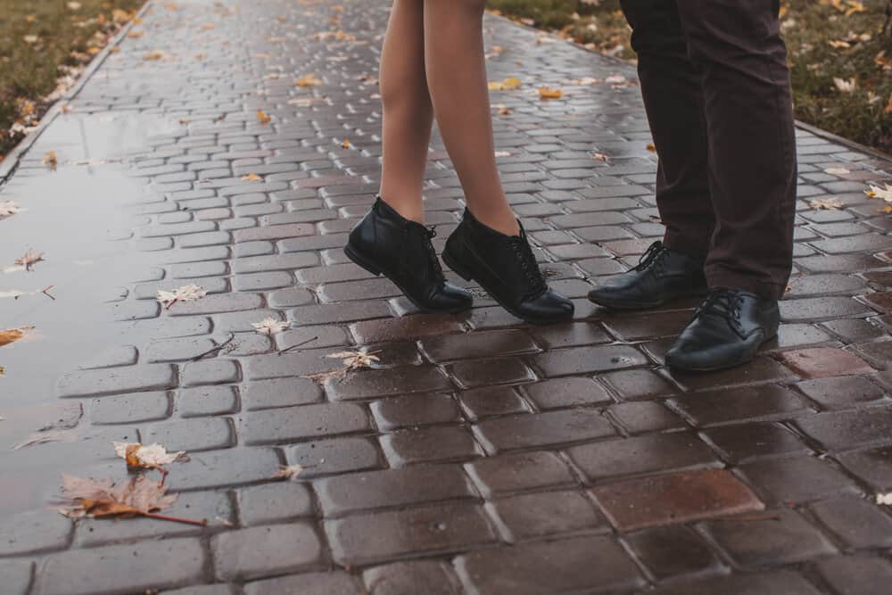 A woman and man's feet on a brick walkway in the rain.