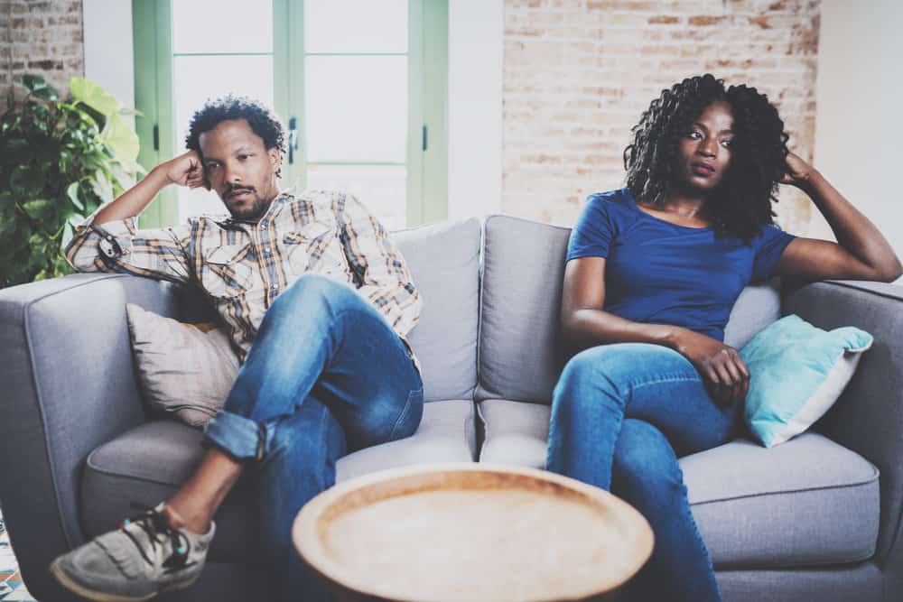 A couple sits on opposite sides of a couch upset.