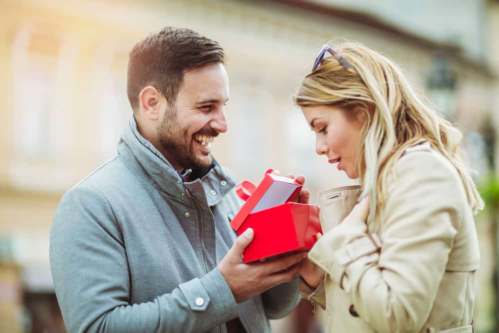A man laughs while giving a gift in a red box to a woman.