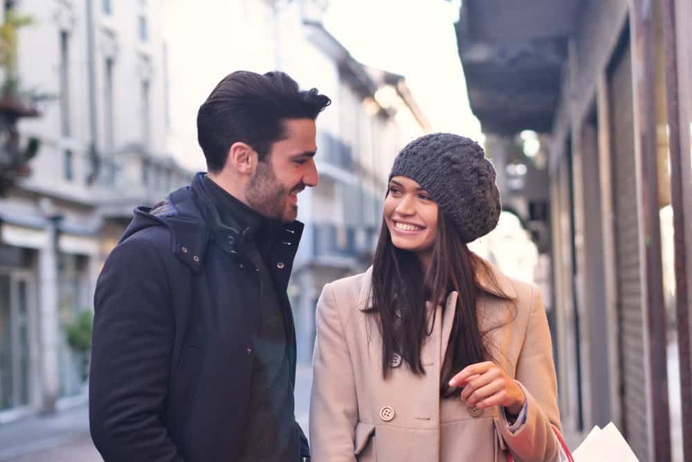 A couple is outdoors smiling at one another.
