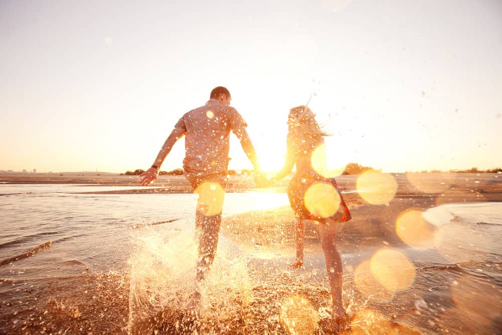 A happy couple runs on the beach under the sun.