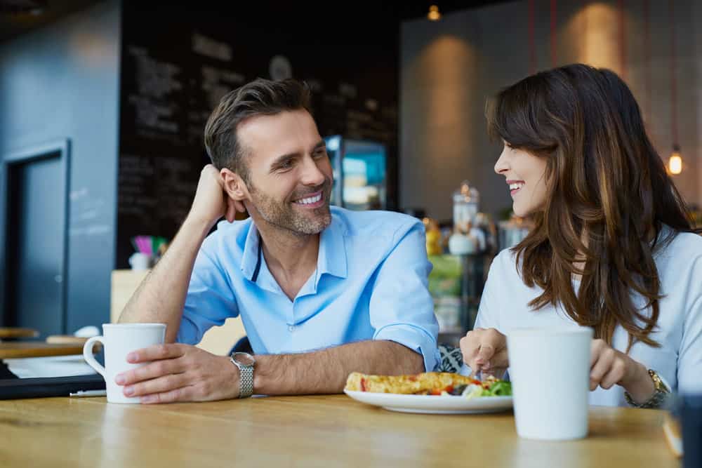 A couple smiles together at lunch because they practice self care in their relationship