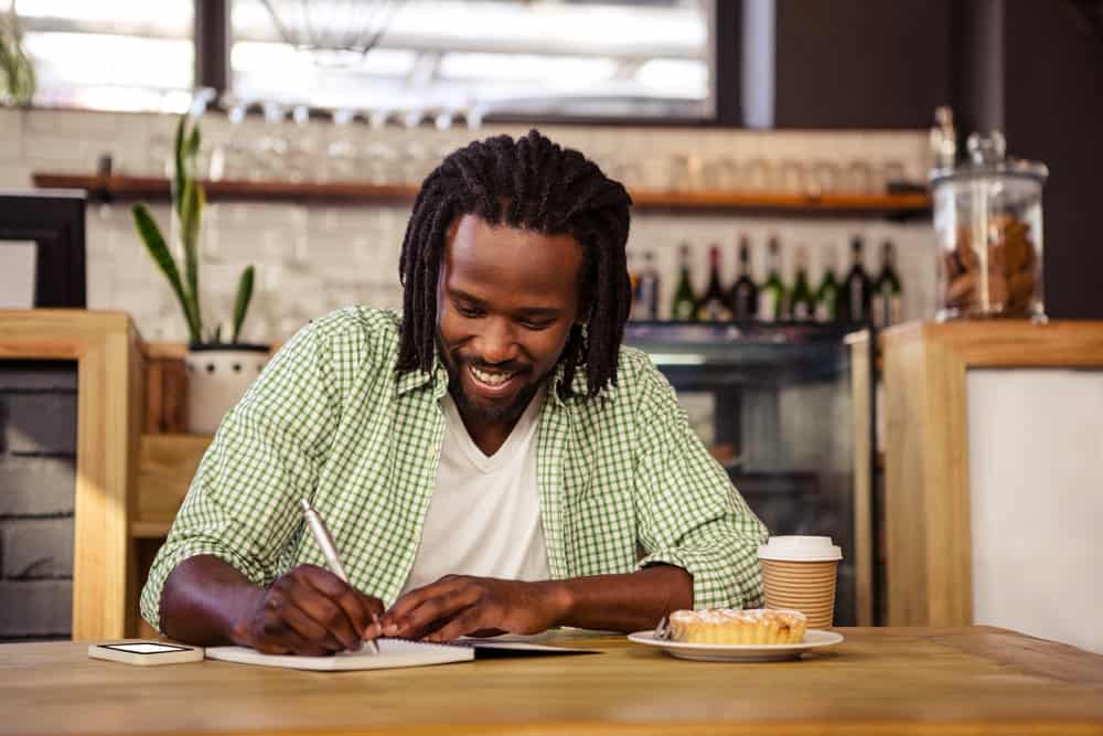 A man happily writes in a cafe, practicing marriage self care