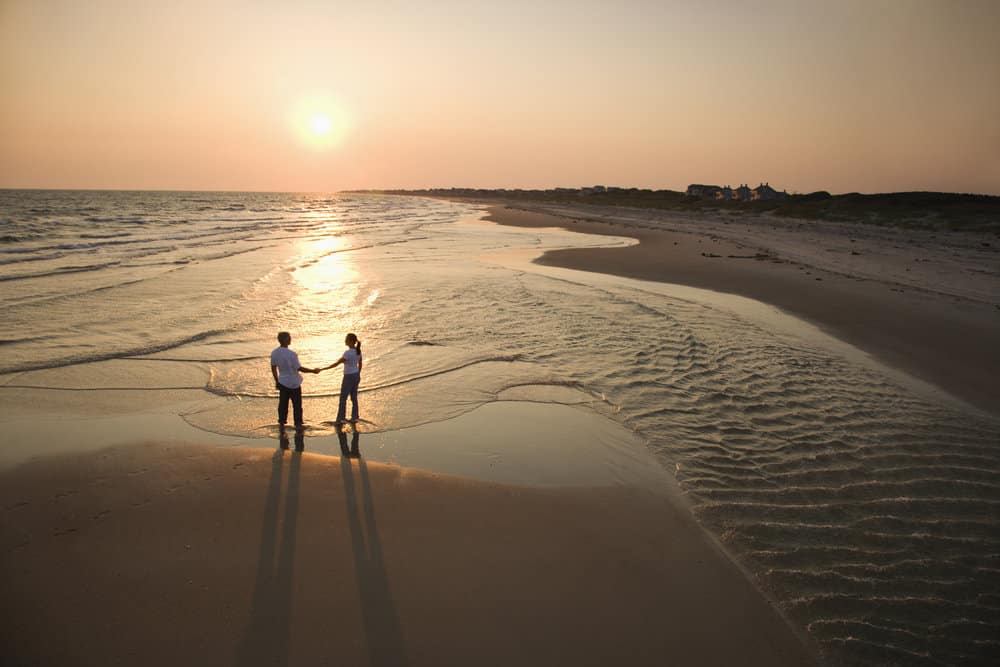 A couple holds hands on the beach at sunset.