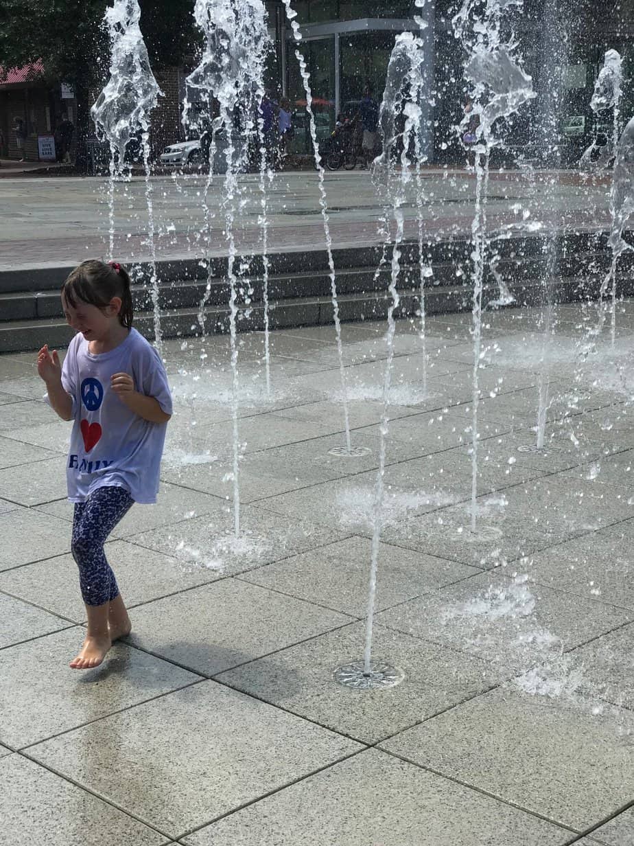 A child plays in a fountain while getting splashed with water.