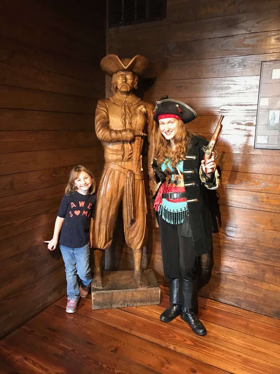 A child poses with a pirate actor next to a statue.