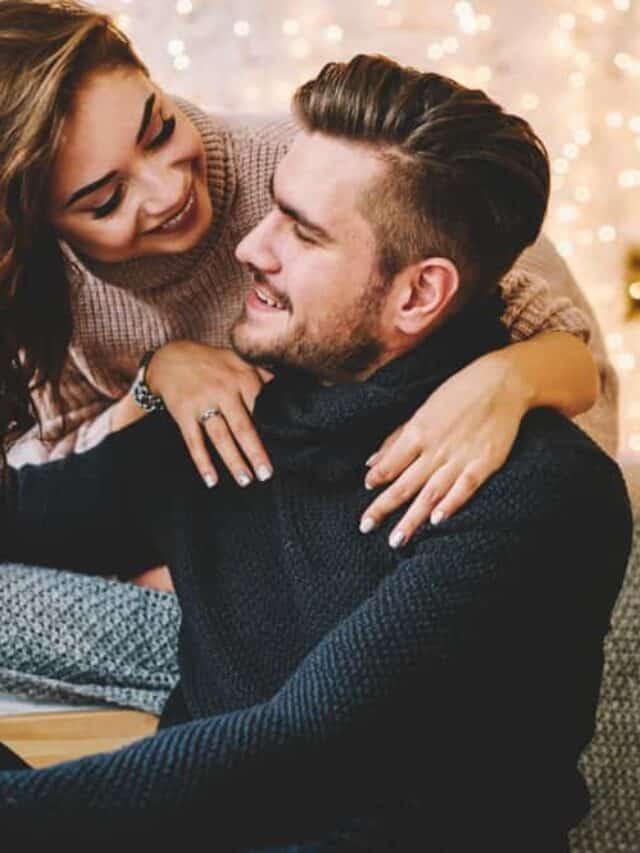 A woman laughs at a man as they smile. Christmas decor is seen behind them.