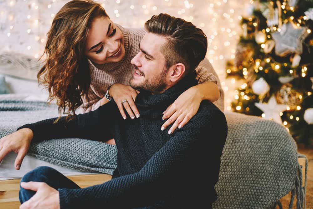 A woman laughs at a man as they smile. Christmas decor is seen behind them.