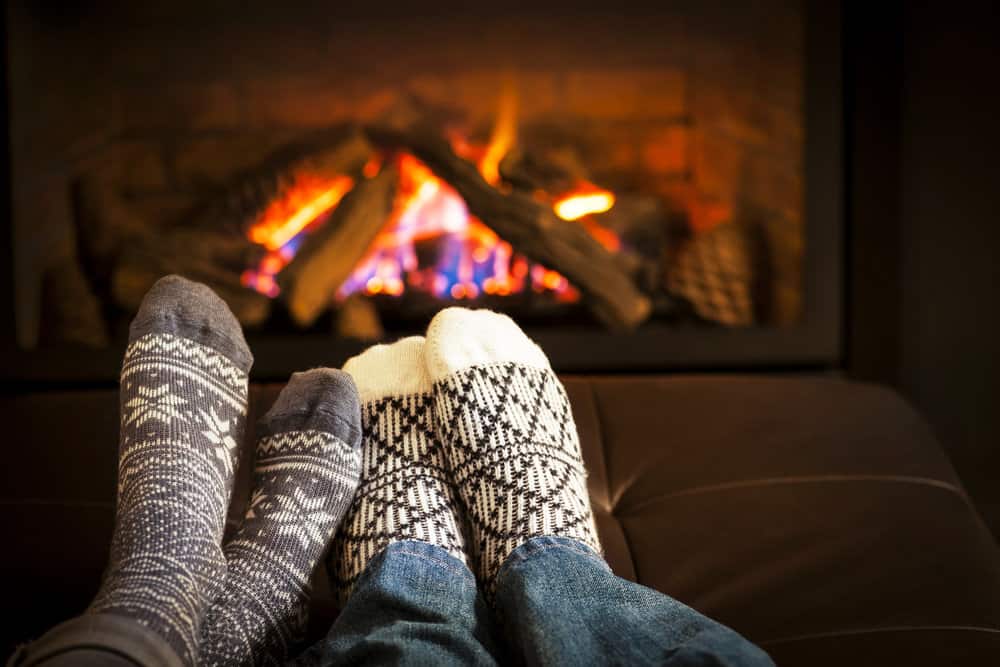 View of two pairs of feet with socks on, with a fireplace behind them.