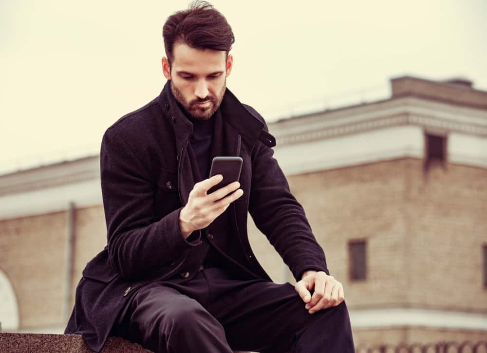 A man sits outside while reading a message on his phone.