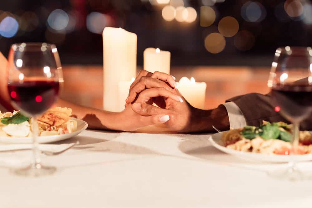 Close up of a couple holding hands at a candlelit dinner.