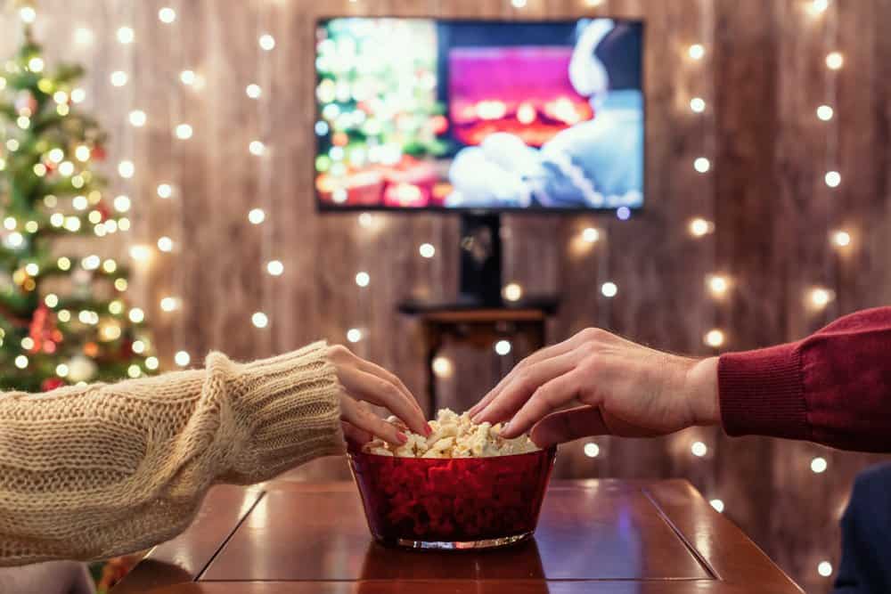 A couple share a bowl popcorn while watching romantic movies at Christmas