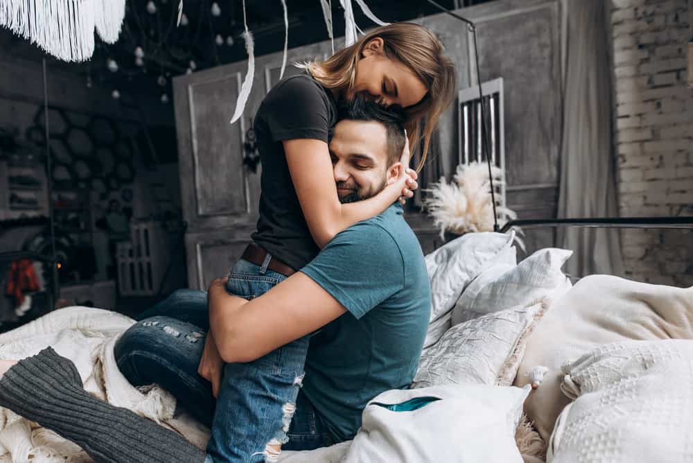 A woman embraces a man on a bed.