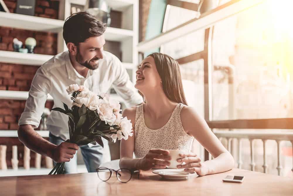 A man giving his partner flowers while being more romantic