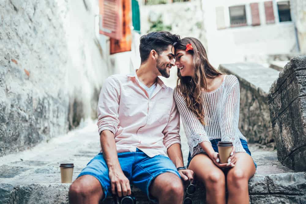 A couple snuggles together in an alley while smiling.