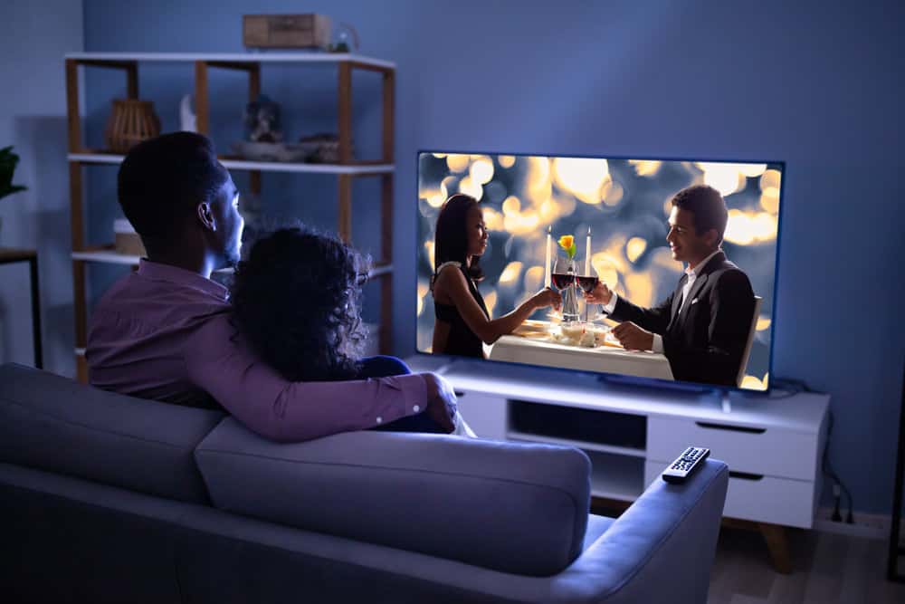 A couple sitting on a couch in their home watching TV at night. 