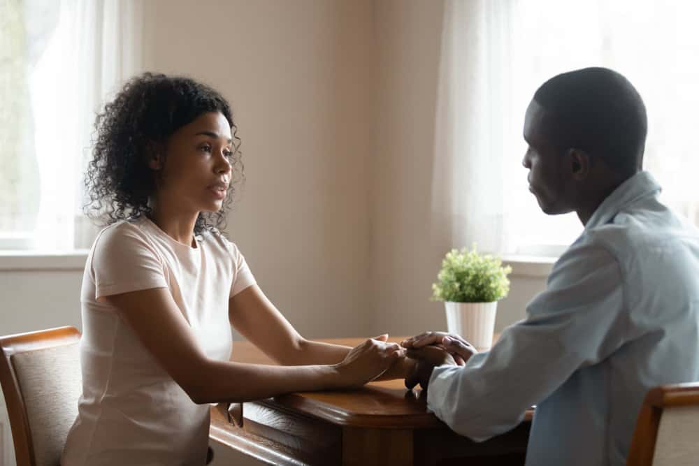 A couple sits across from each other at a table with serious expressions while chatting.