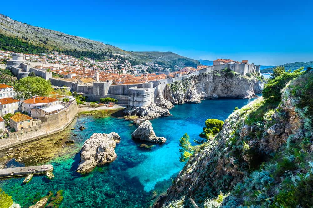 A panoramic view of a romantic European babymoon destination with turquoise blue waters, a rocky cliff, and deep blue sky
