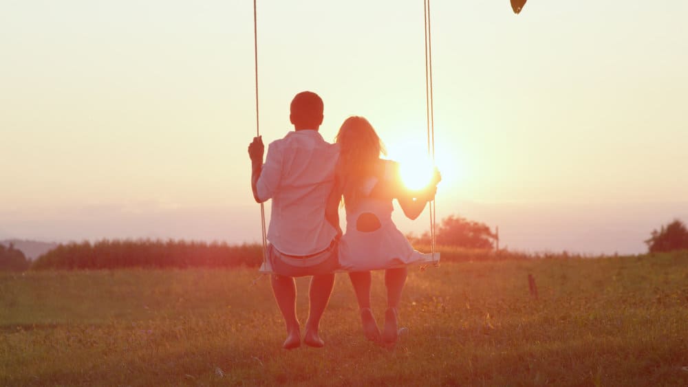 A couple shares a swing during a romantic sunset while discussing their expectations in relationships