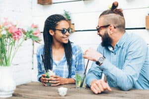 A couple asking Never Have I Ever Questions for Couples is smiling as they sit at a table outside