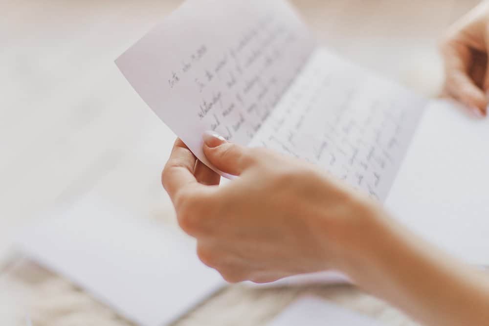 A tropical up image of a woman's hands as she reads love reports for her written in cursive.