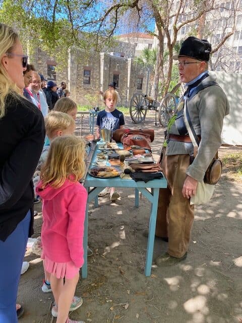 A reenactor explains historical props placed on a table to a group of visitors at the Alamo in San Antonio, Texas.