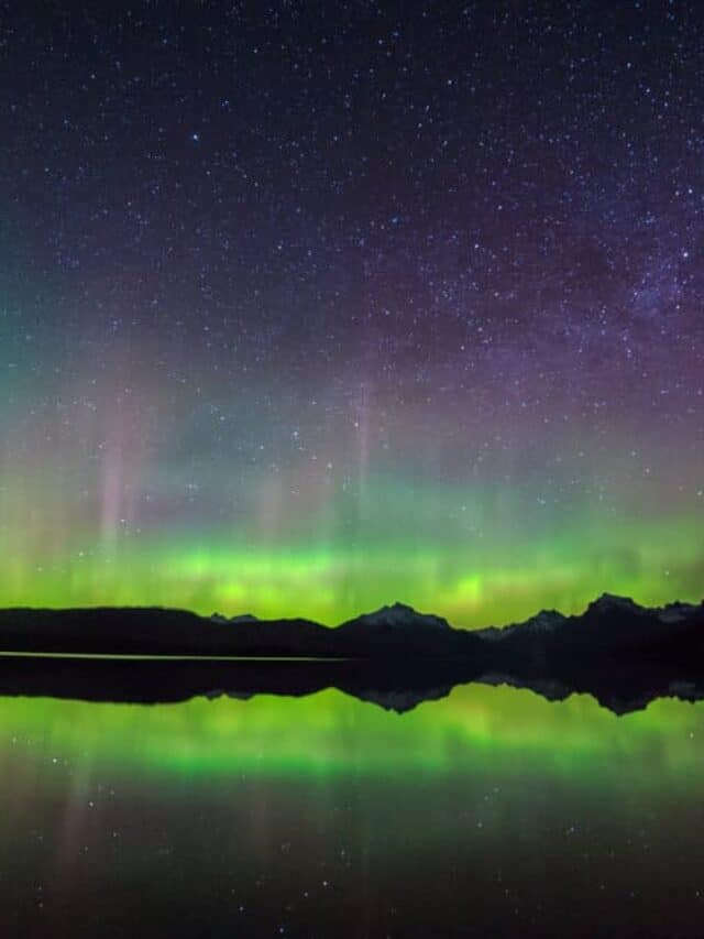 A purple and green sky reflected in a lake in Montana, one of the best places to see the Northern Lights in the USA
